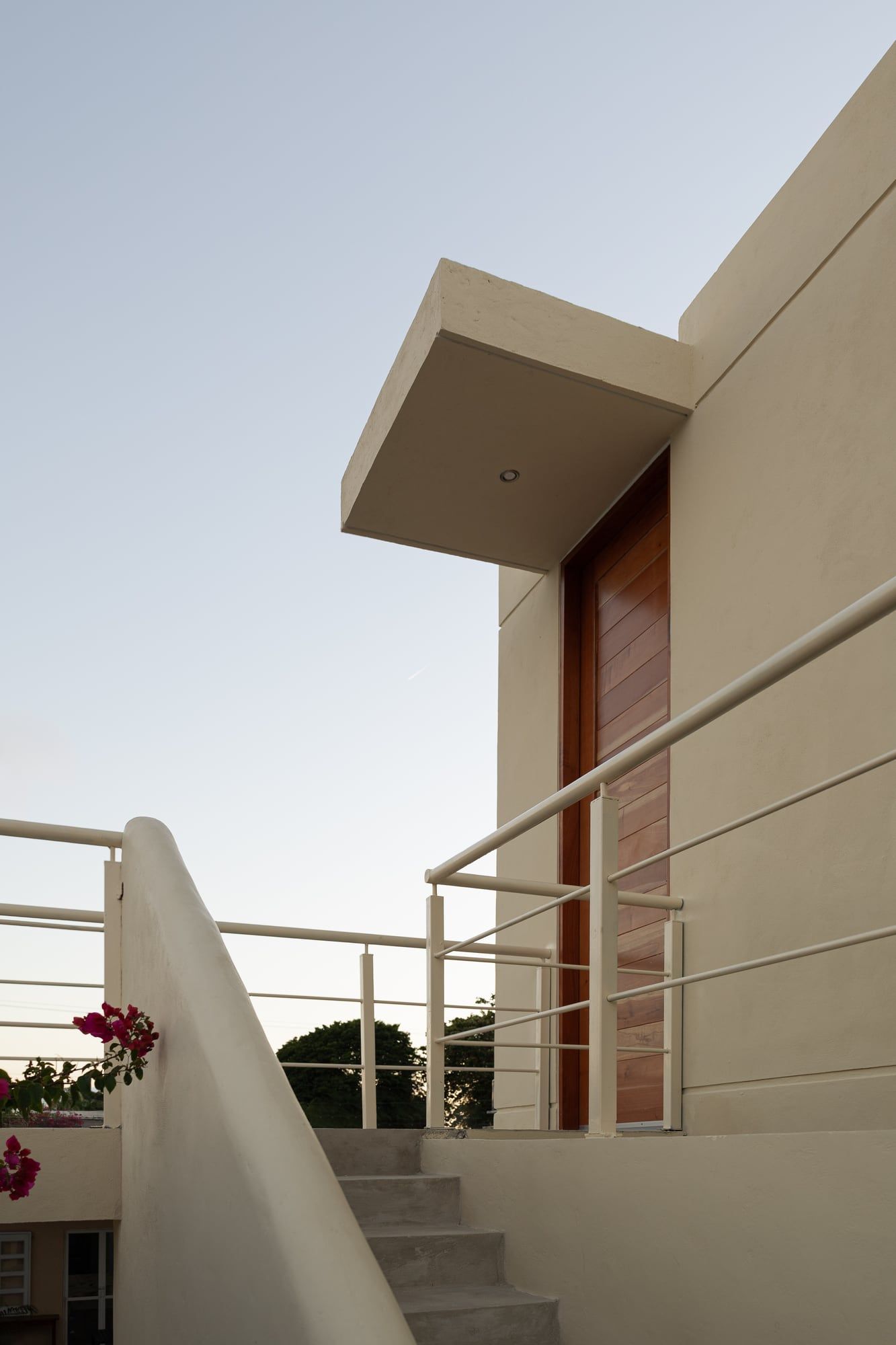 Entrada con puerta de madera, escalera y barandal al atardecer