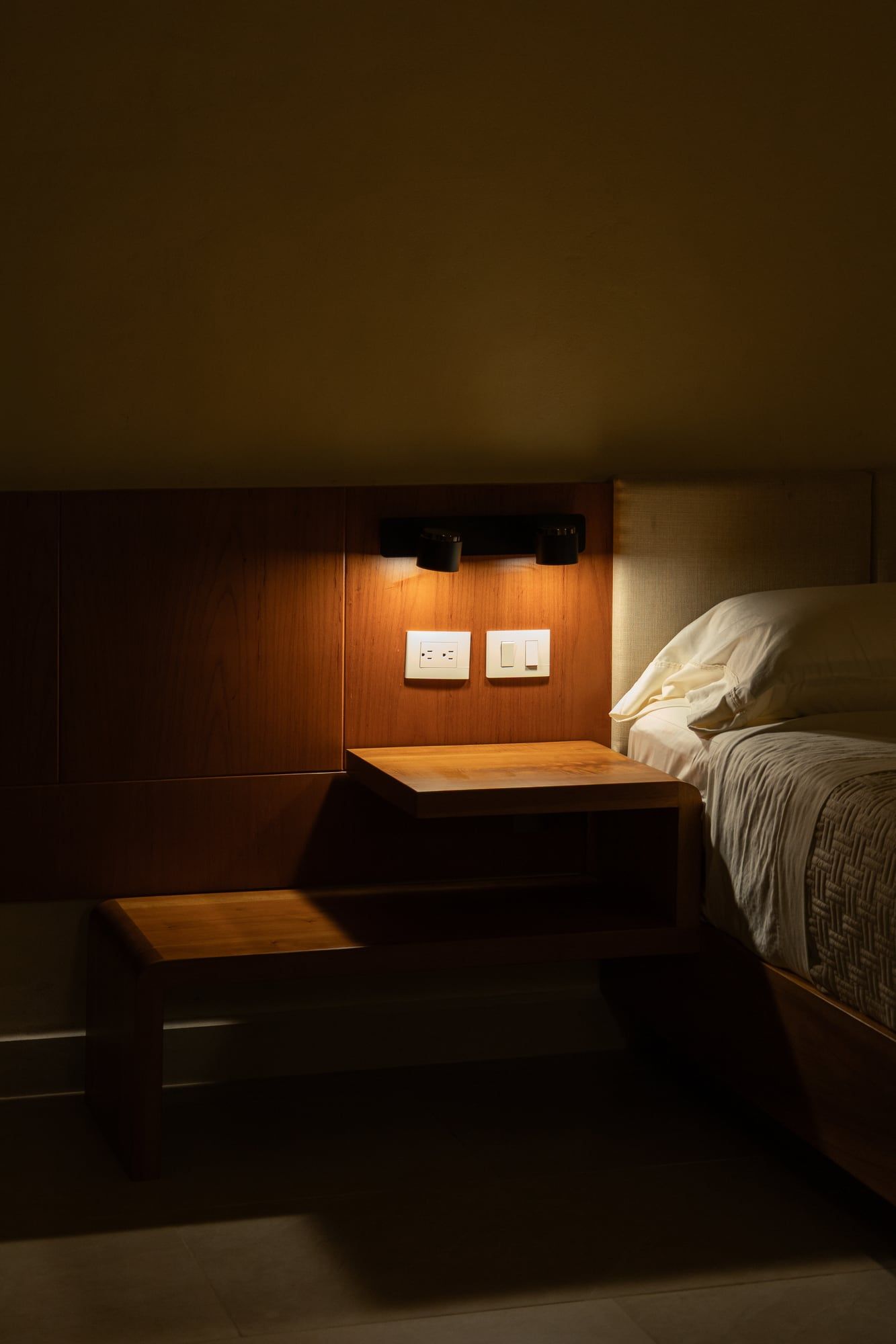 Buró de madera con lámpara de lectura junto a la cabecera de una cama